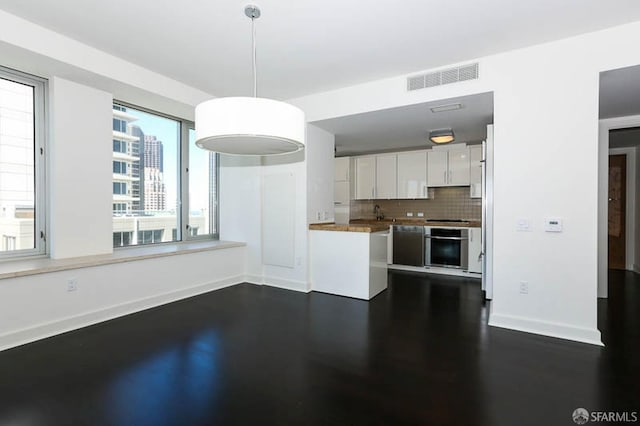 kitchen featuring baseboards, visible vents, oven, white cabinets, and backsplash