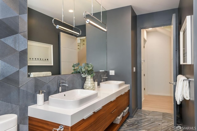 full bathroom featuring double vanity, toilet, decorative backsplash, and a sink