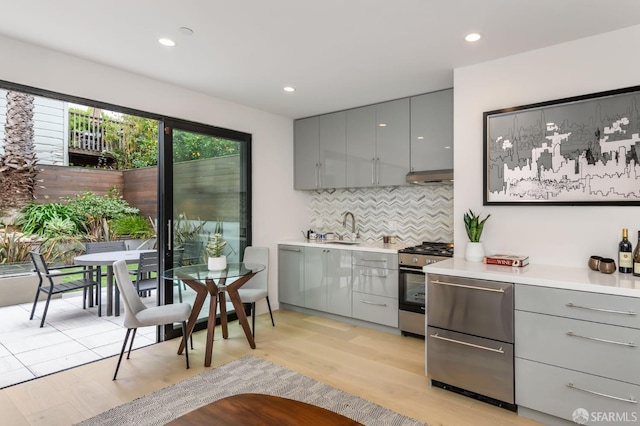 kitchen featuring under cabinet range hood, a sink, light countertops, stainless steel range with gas cooktop, and gray cabinets