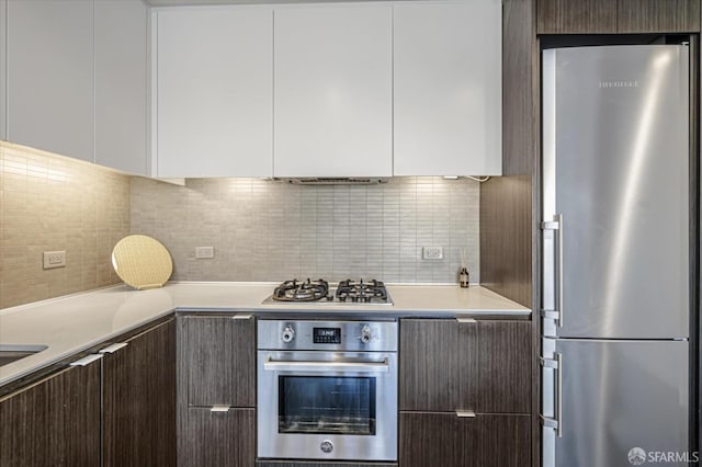 kitchen with white cabinets, decorative backsplash, stainless steel appliances, and dark brown cabinetry