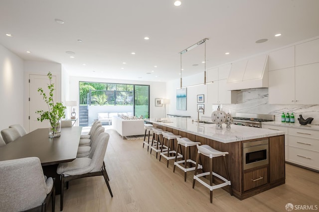 3537 23rd St Unit A, San Francisco, CA 94110 - kitchen featuring stainless steel microwave, a breakfast bar, custom range hood, a sink, and white cabinetry