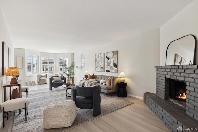 living room featuring light wood-style floors, a brick fireplace, and baseboards