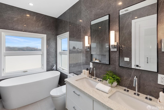 bathroom with tile walls, vanity, a washtub, toilet, and tile patterned floors