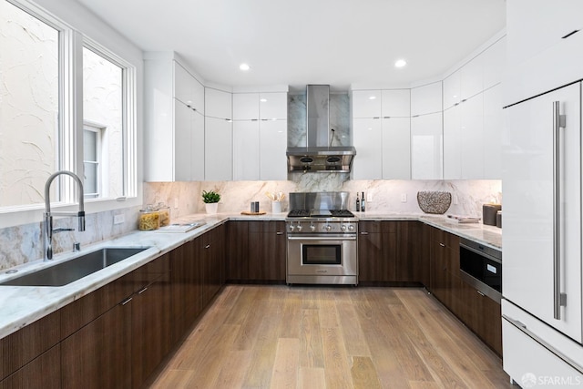 kitchen featuring sink, high end appliances, light hardwood / wood-style flooring, wall chimney range hood, and white cabinetry