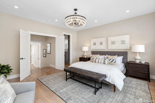 bedroom with light wood-type flooring, ensuite bath, and a chandelier