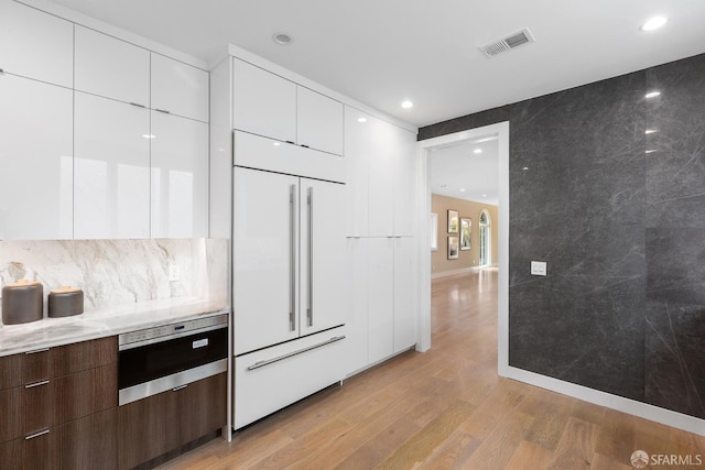 kitchen with white cabinets, light hardwood / wood-style flooring, oven, dark brown cabinetry, and paneled fridge