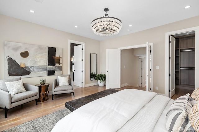 bedroom featuring light wood-type flooring, a chandelier, and a walk in closet