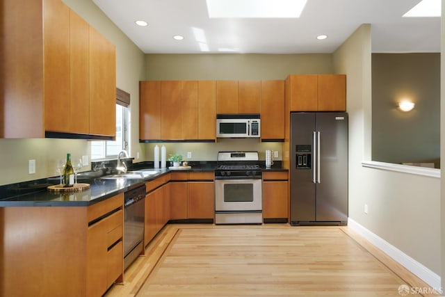 3310 19th St Unit 303, San Francisco, CA 94110 - kitchen with stainless steel appliances, a sink, light wood-style floors, dark countertops, and brown cabinetry