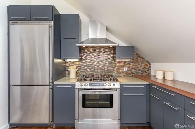 kitchen with wooden counters, vaulted ceiling, appliances with stainless steel finishes, decorative backsplash, and wall chimney range hood