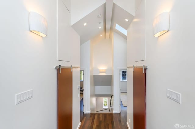 hallway with a barn door, dark hardwood / wood-style floors, high vaulted ceiling, and beam ceiling