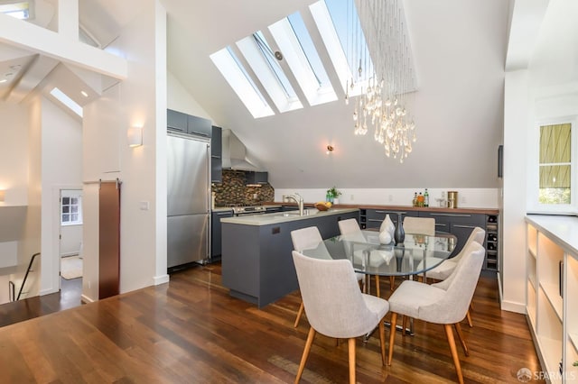 dining area featuring dark wood-type flooring, sink, an inviting chandelier, a skylight, and high vaulted ceiling