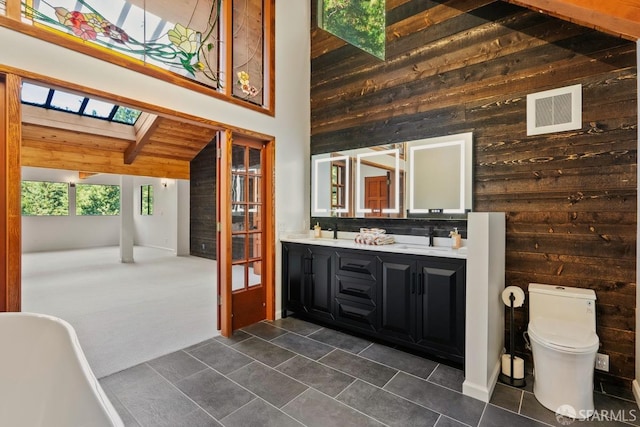 bathroom with vanity, a skylight, toilet, wooden walls, and tile patterned flooring