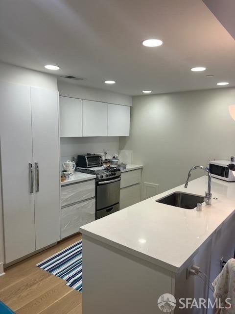 kitchen with light wood-type flooring, white cabinetry, sink, and stainless steel range with electric stovetop