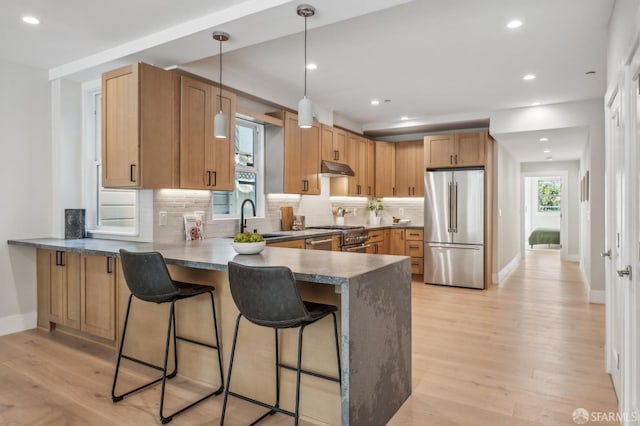 kitchen featuring a breakfast bar, a peninsula, light wood-style flooring, a sink, and appliances with stainless steel finishes