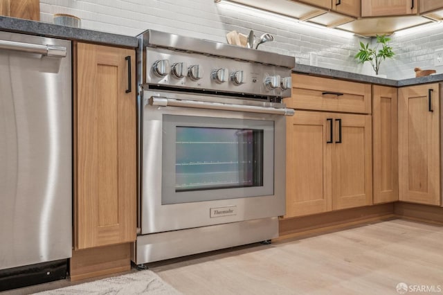 kitchen featuring tasteful backsplash, appliances with stainless steel finishes, dark stone counters, and light wood-style floors