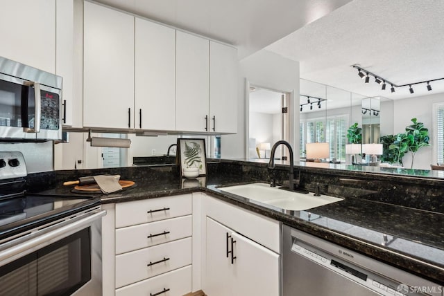 kitchen featuring a sink, track lighting, white cabinets, dark stone countertops, and stainless steel appliances