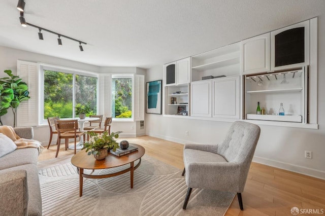 living room featuring baseboards, rail lighting, light wood-style floors, and a textured ceiling