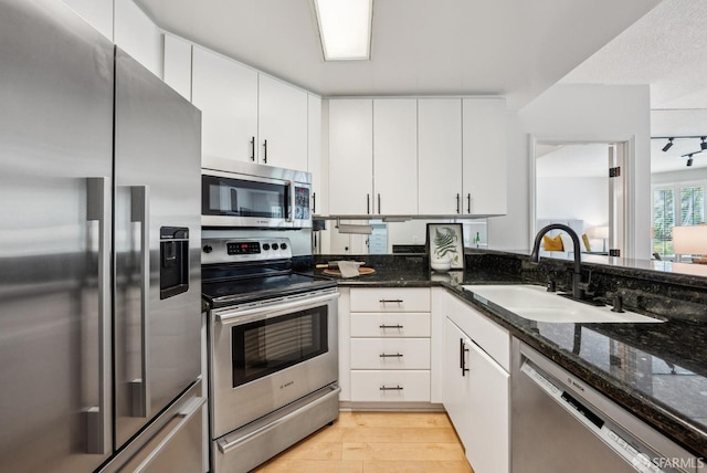 kitchen featuring light wood-type flooring, white cabinetry, a sink, dark stone countertops, and stainless steel appliances