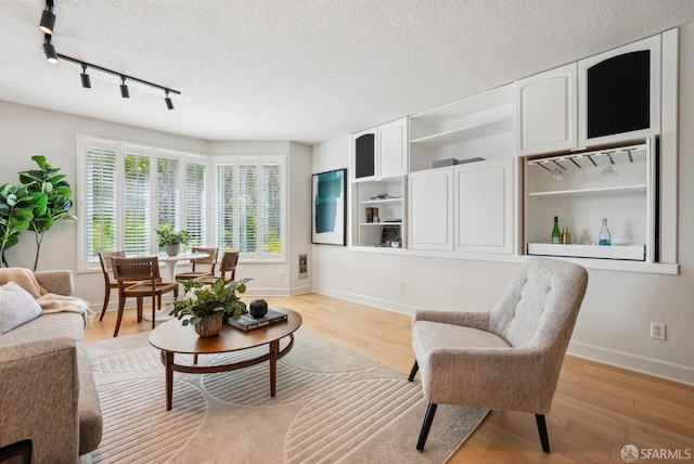 living room featuring light wood-style floors, track lighting, baseboards, and a textured ceiling