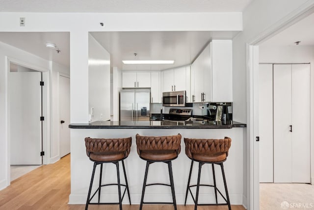 kitchen featuring a peninsula, dark countertops, appliances with stainless steel finishes, and light wood-style flooring