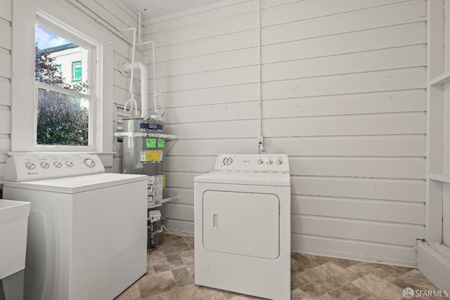 clothes washing area with laundry area, stone finish flooring, washer and clothes dryer, and strapped water heater