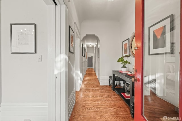 hall with arched walkways, light wood-style flooring, and baseboards