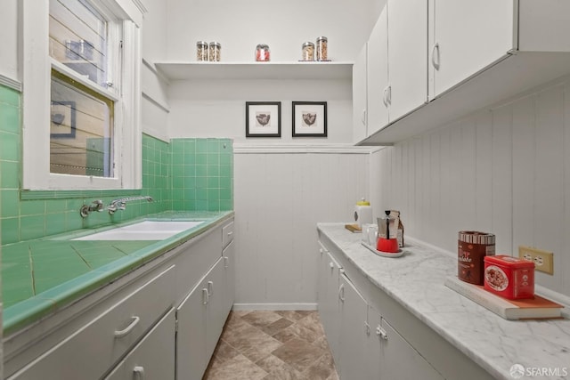 kitchen featuring a wainscoted wall, a sink, white cabinetry, and decorative backsplash