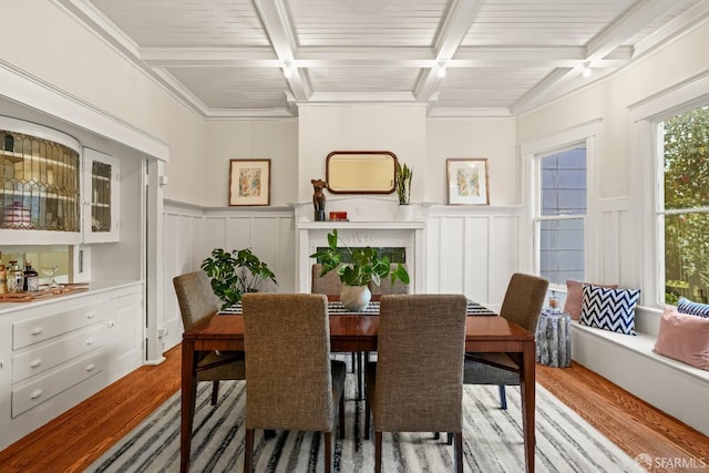 dining area with a wainscoted wall, wood finished floors, and beamed ceiling