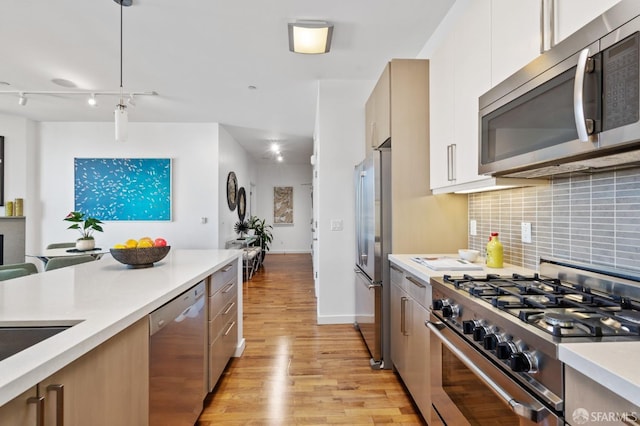 kitchen featuring pendant lighting, appliances with stainless steel finishes, light wood-type flooring, tasteful backsplash, and rail lighting