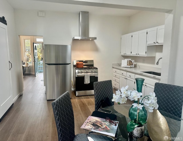 kitchen with white cabinetry, sink, wall chimney exhaust hood, stainless steel appliances, and light hardwood / wood-style flooring