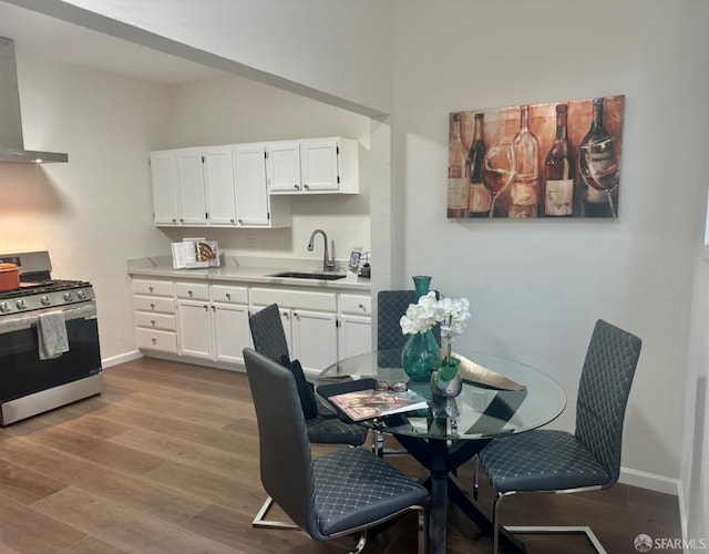 kitchen featuring white cabinetry, sink, stainless steel range with gas stovetop, light wood-type flooring, and wall chimney exhaust hood