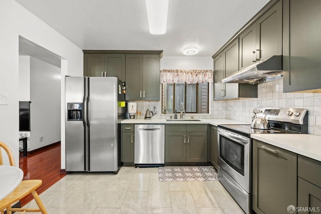 kitchen with appliances with stainless steel finishes, under cabinet range hood, light countertops, a sink, and backsplash