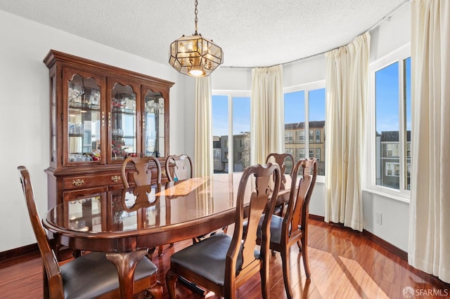 dining area featuring light wood finished floors, baseboards, an inviting chandelier, and a textured ceiling