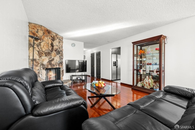 living room featuring a stone fireplace, a textured ceiling, and wood finished floors