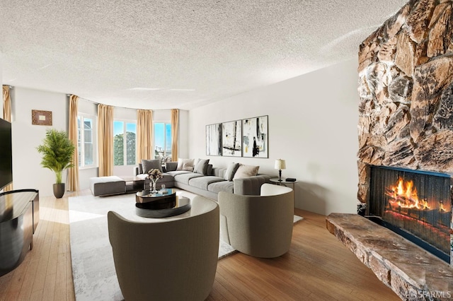 living room with a textured ceiling, a stone fireplace, and hardwood / wood-style flooring