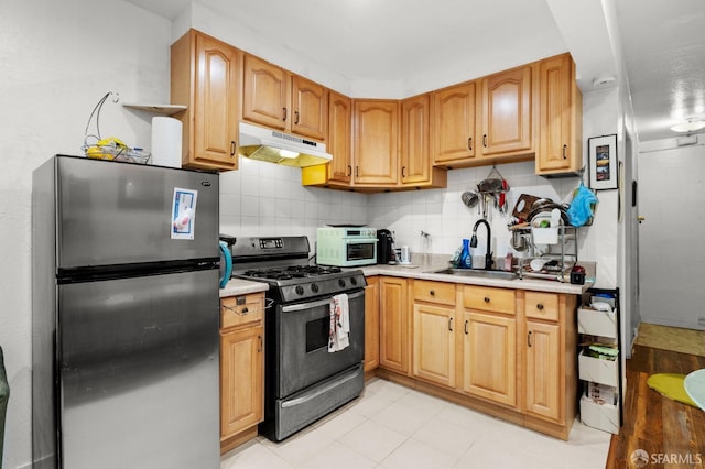 kitchen featuring freestanding refrigerator, under cabinet range hood, light countertops, a sink, and range with gas cooktop
