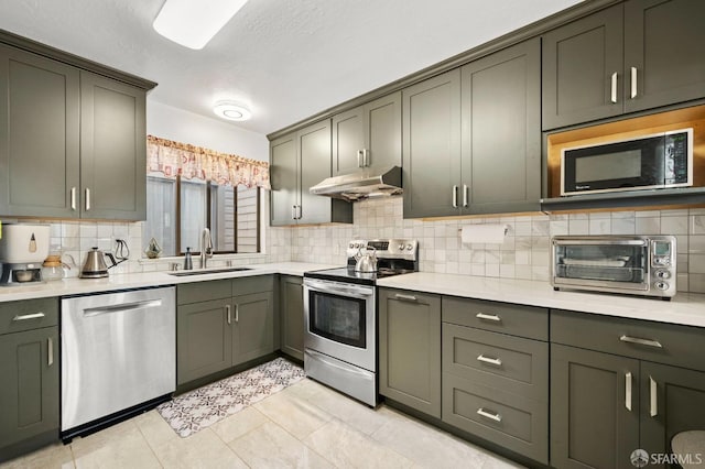 kitchen featuring appliances with stainless steel finishes, a toaster, under cabinet range hood, decorative backsplash, and a sink