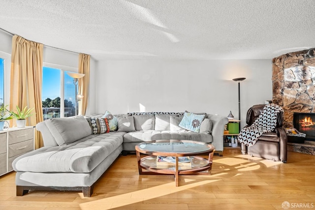 living room featuring a textured ceiling, a stone fireplace, and light wood-type flooring
