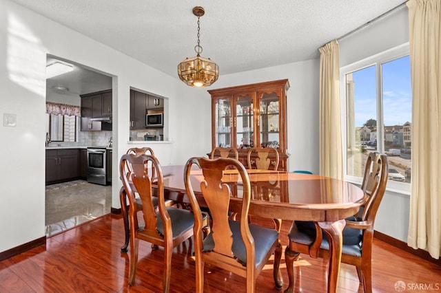 dining space with a notable chandelier, baseboards, a textured ceiling, and dark wood finished floors