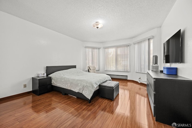 bedroom with light wood-style floors, a baseboard heating unit, baseboards, and a textured ceiling