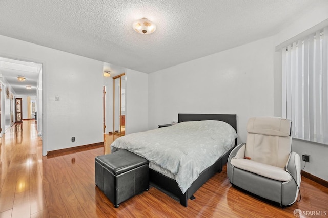 bedroom with baseboards, wood finished floors, and a textured ceiling