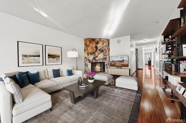 living room featuring a stone fireplace, a textured ceiling, and wood finished floors