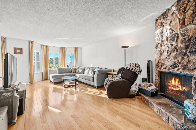 living room featuring a stone fireplace, a textured ceiling, and wood finished floors