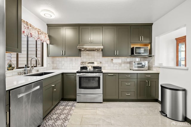kitchen featuring light countertops, under cabinet range hood, decorative backsplash, stainless steel appliances, and a sink