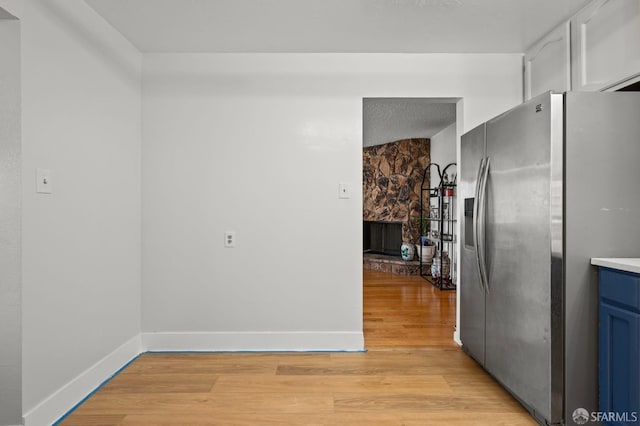 kitchen featuring light wood finished floors, baseboards, blue cabinets, and stainless steel fridge