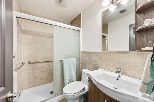 bathroom featuring visible vents, toilet, tile walls, a shower stall, and vanity