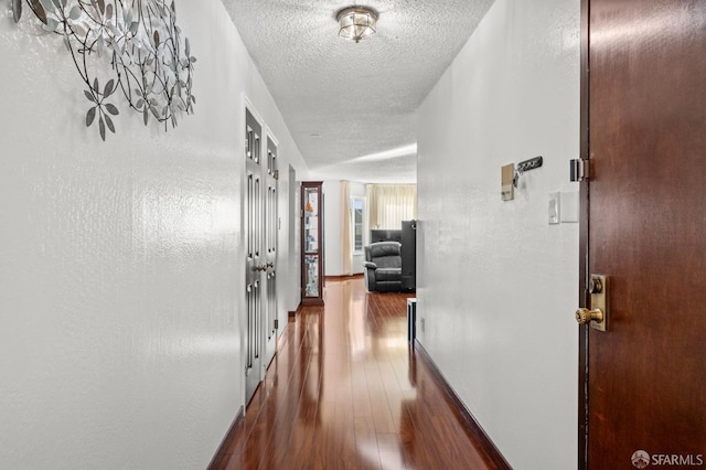 corridor featuring dark wood-type flooring, a textured ceiling, and baseboards