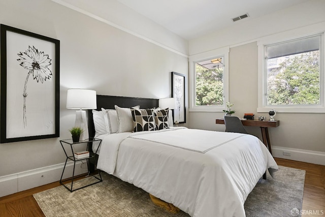 bedroom with baseboards, visible vents, and wood finished floors