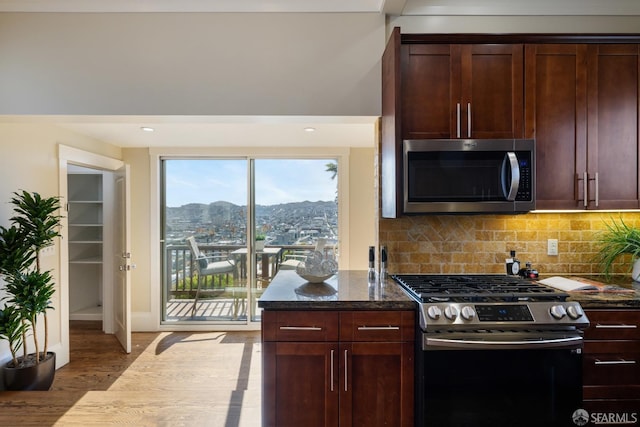 kitchen featuring dark stone countertops, a mountain view, appliances with stainless steel finishes, backsplash, and light wood-style floors