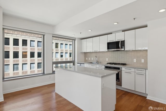 kitchen with a sink, wood finished floors, white cabinetry, appliances with stainless steel finishes, and decorative backsplash